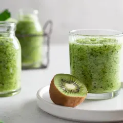 Zielony koktajl w szklance i butelkach, z połówkami kiwi na talerzyku.