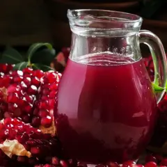 Dzbanek soku z granatów i rozkrojone granaty na drewnianym stole.